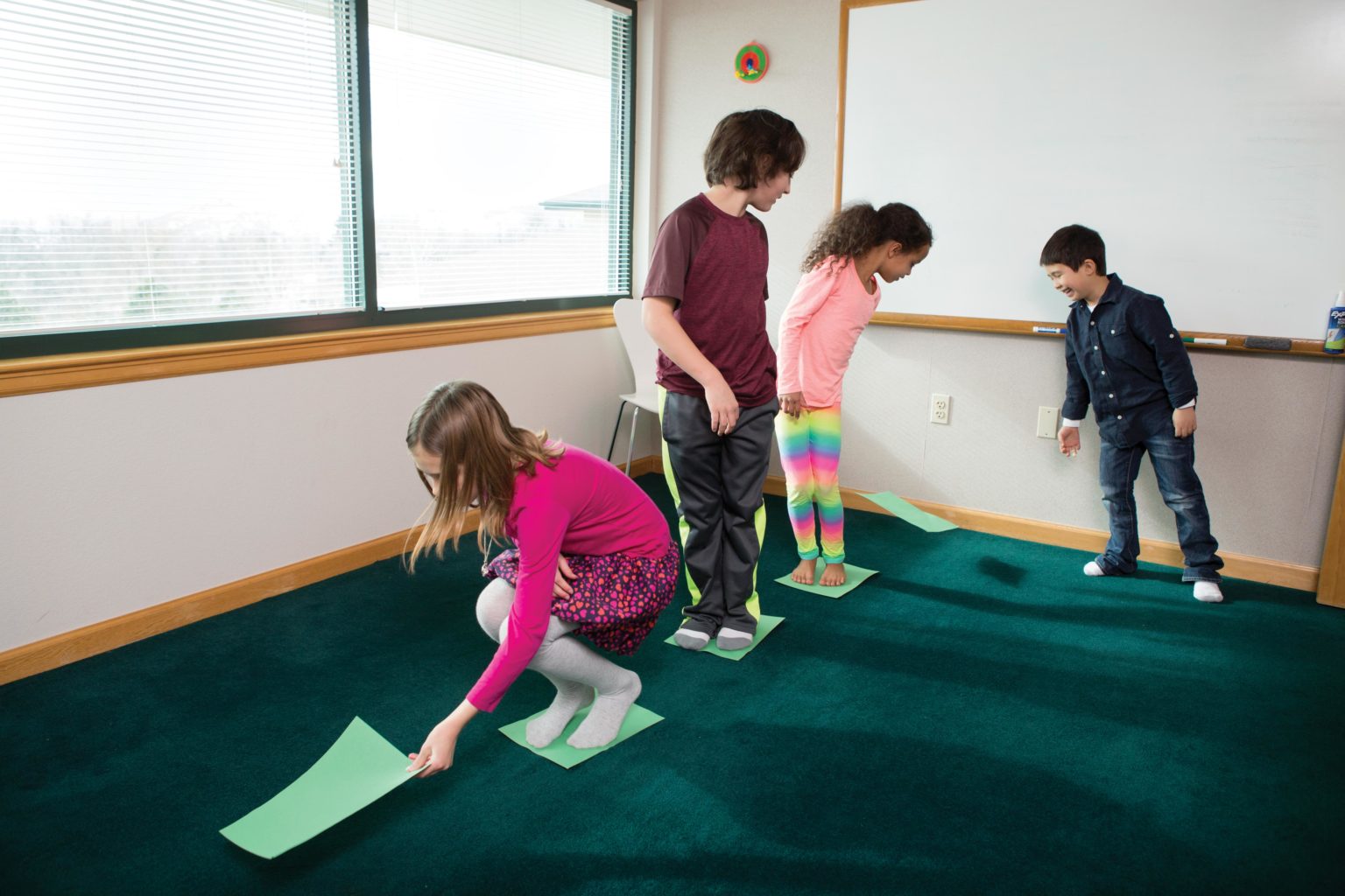 Children in a line, placing green paper on the ground as stepping stones.