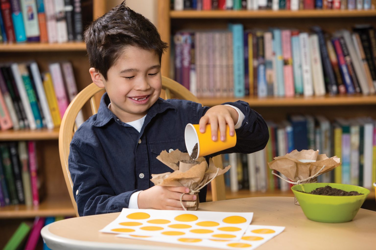 Elementary boy sitting at a table as he pours potting soil into a paper towel roll.