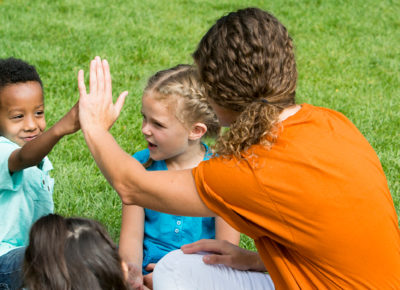 A volunteer who is successfully implementing curriculum gives a preschooler a high five.