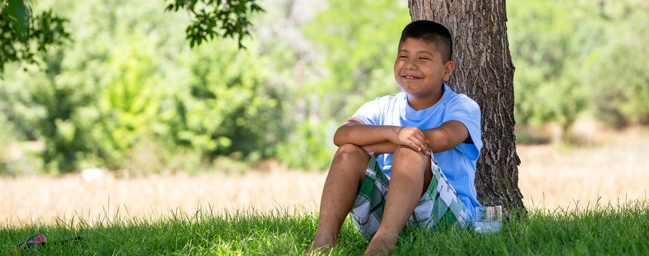 A boy sits outside under a tree to think about taking care of God's world.
