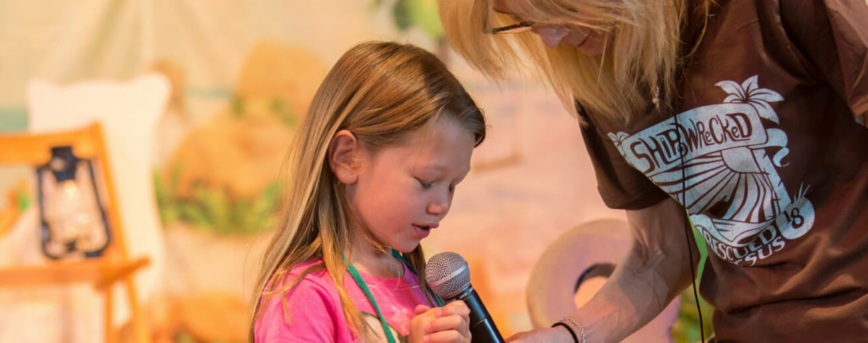 An elementary aged girl prays into a microphone.