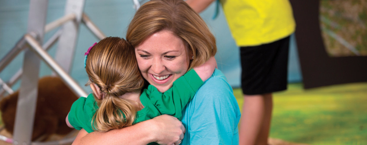 A young female volunteer hugs an early elementary girl.