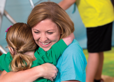 A young female volunteer hugs an early elementary girl.