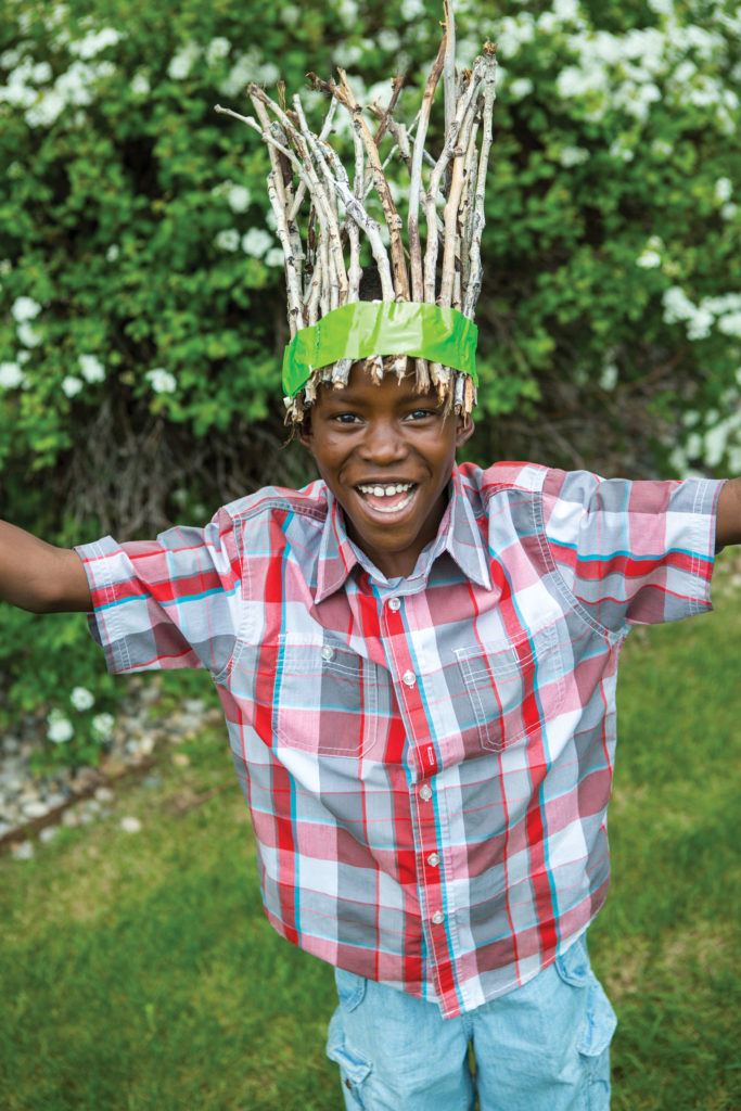 A boy smiling with a crown made of sticks and duct tape.