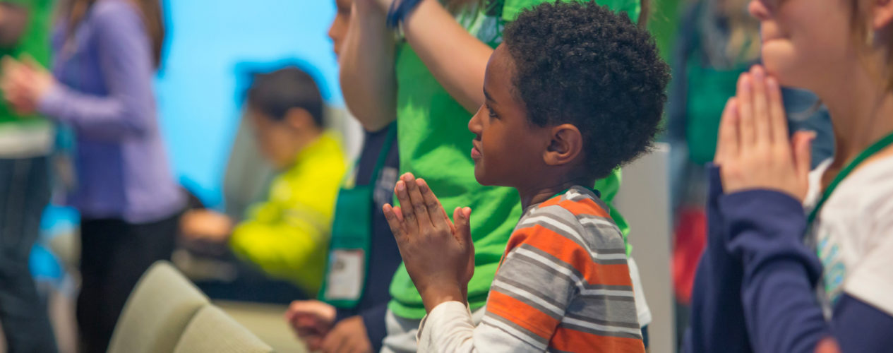 An elementary-aged boy standing in a sanctuary with his hands folded in a time of prayer.