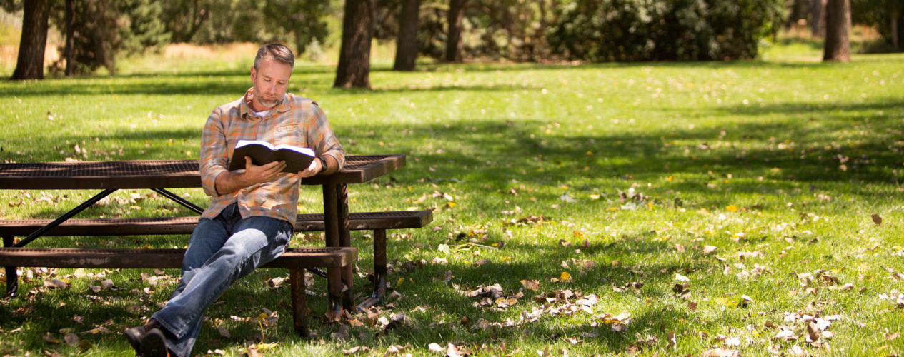 A children's ministry leader maintaining his boundaries by reading his Bible sitting at a picnic table.
