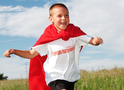 A boy runs through a field dressed as a superhero.
