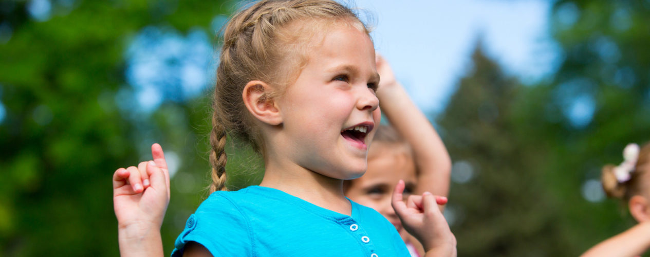 Little girl wearing a blue shirt celebrating outside
