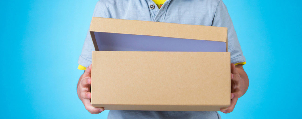 A boy holding a shoe box with the lid cracked open in front of a bright blue background.