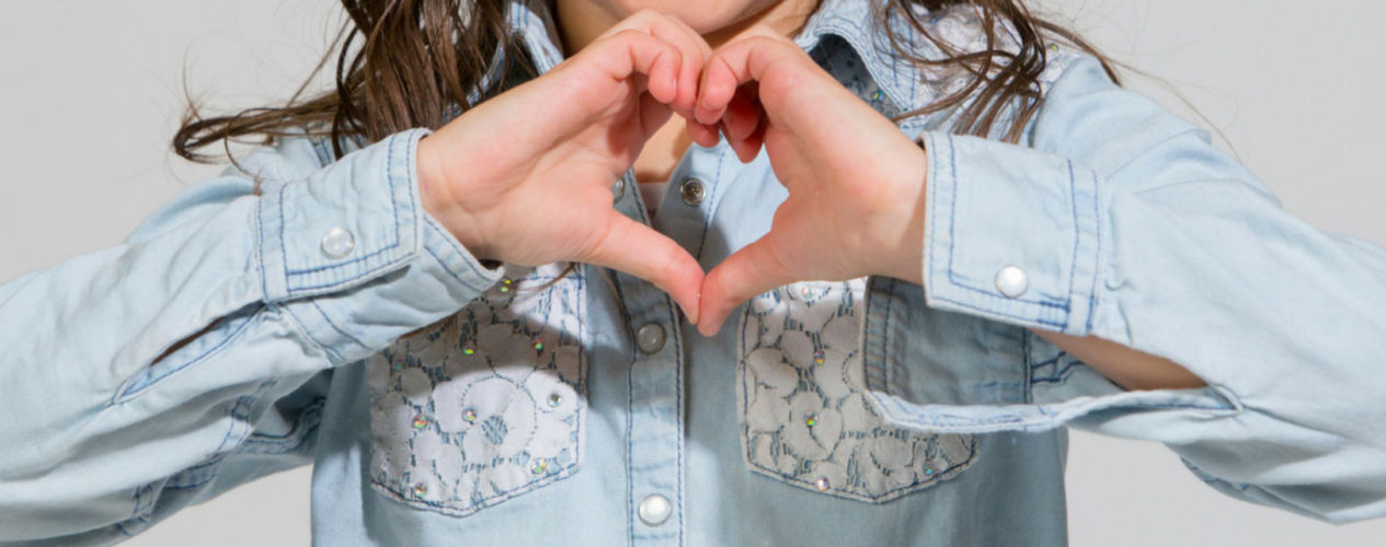 Little girl wearing denim and lace shirt making a heart with her hands.