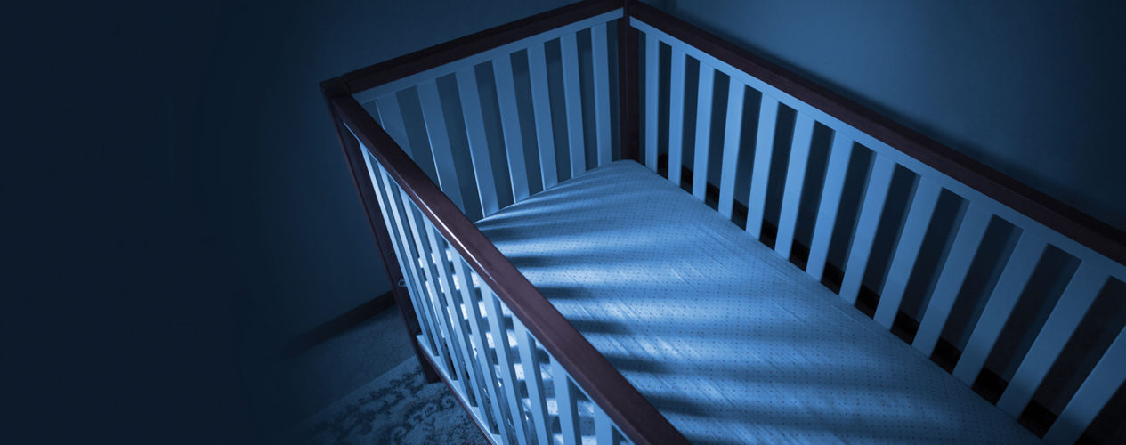 An empty crib in the lighting of night. It's dark with a very deep blue lighting.