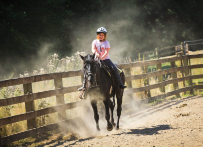 A girl rides horseback and dust flies through the air.
