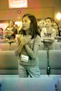 Preteen girl standing with her hands on her heart. She is singing.