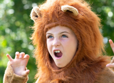 A young girl wearing a lion Halloween custom roars with her hands up like claws.