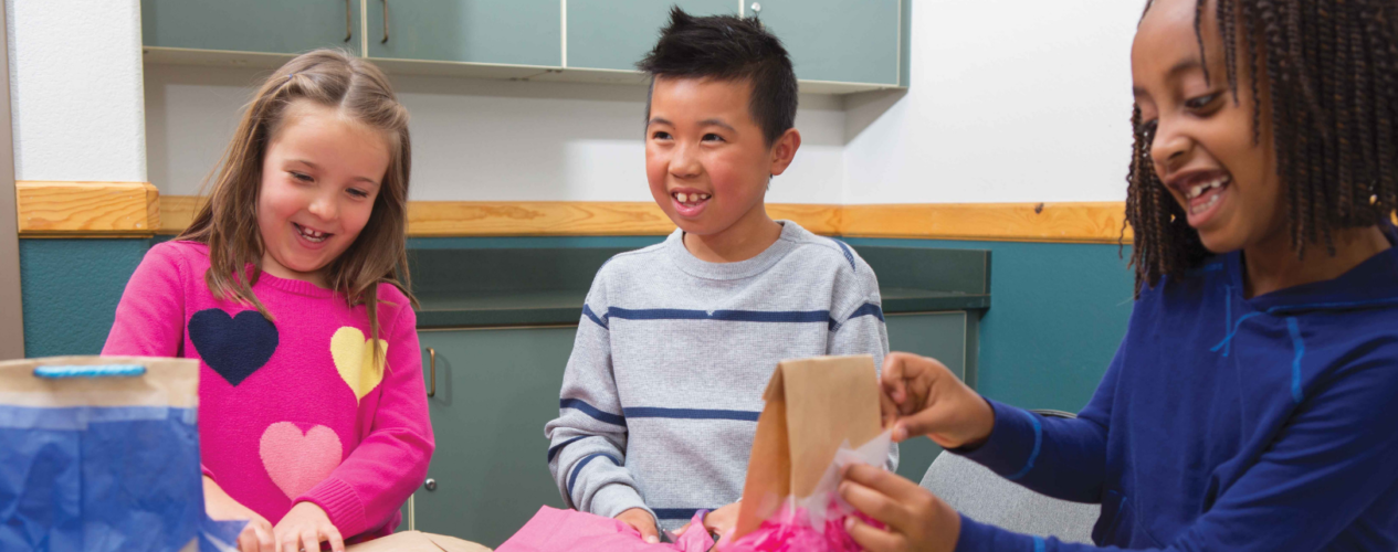 Elementary kids at a table creating paper bag pinatas.