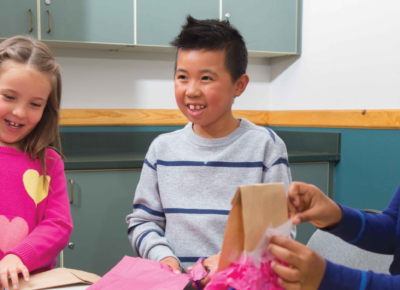 Elementary kids at a table creating paper bag pinatas.