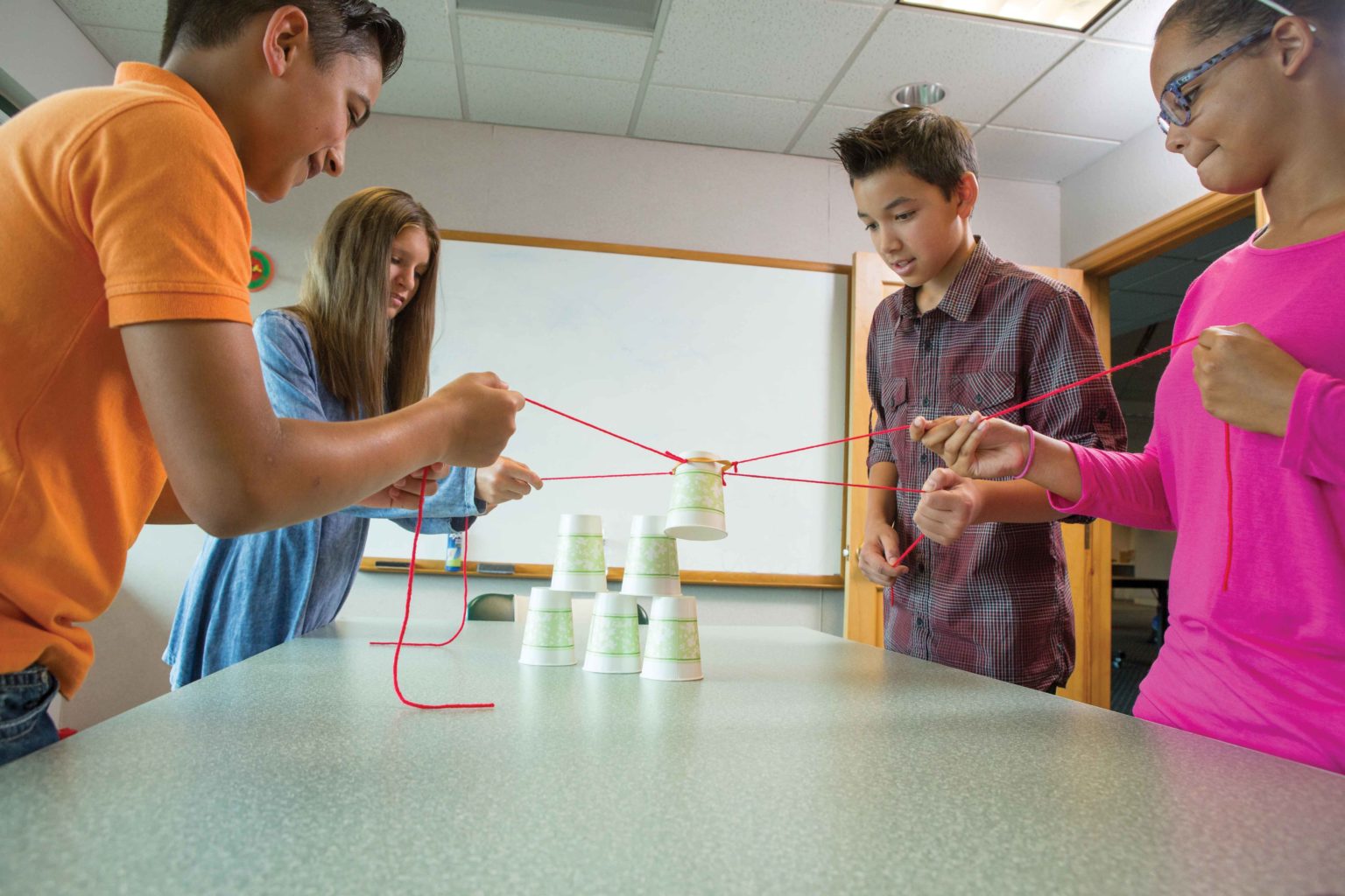 Kids using the yarn and rubber band set up to stack the paper cups.