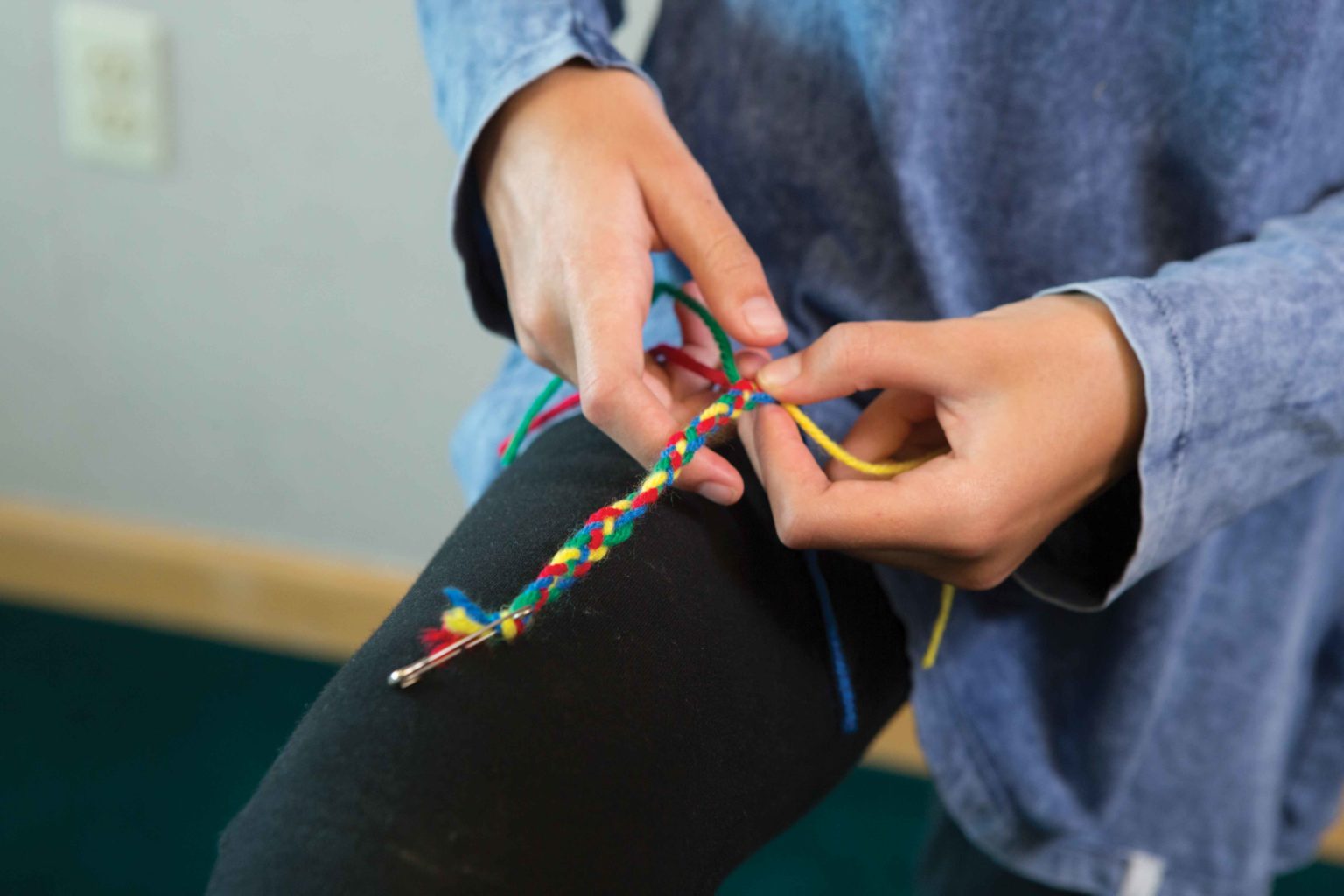 Four strings of colorful yarn being braided by a child.