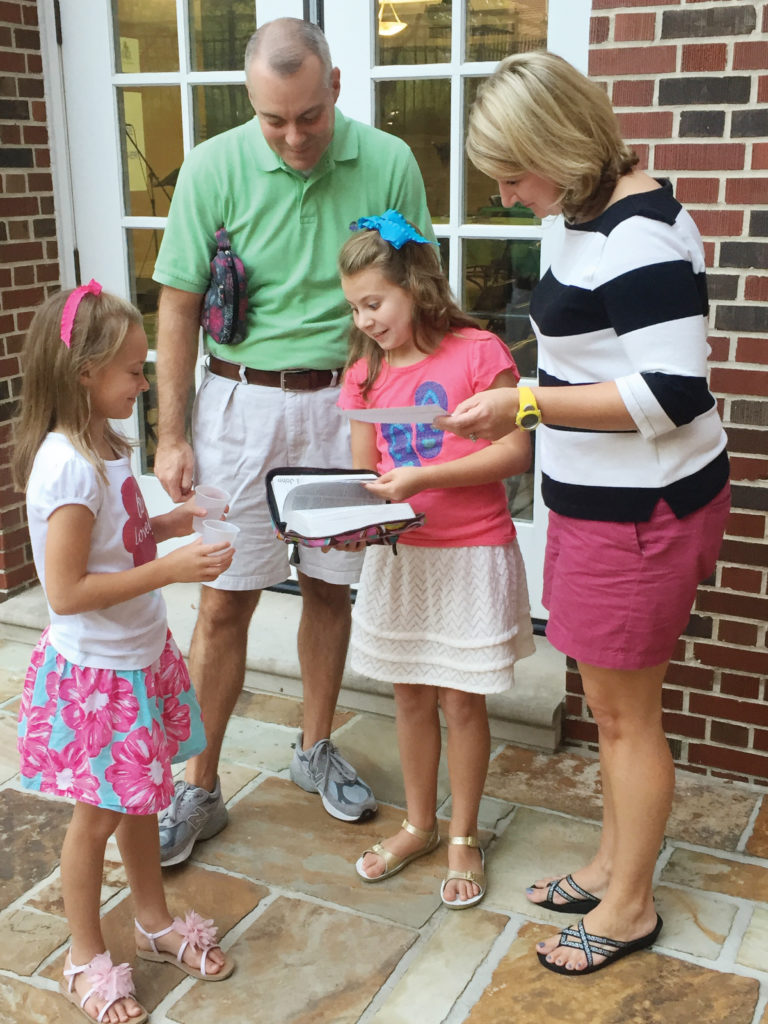 A family of four is standing outside the church, with Bibles in hand, for a family worship experience.