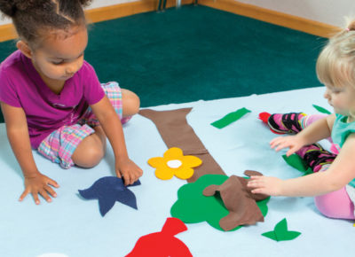 Two preschool-aged girls creating an outdoor scene with felt shapes.