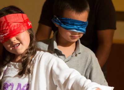 Two children in blindfolds walking in a line for a Christmas game.