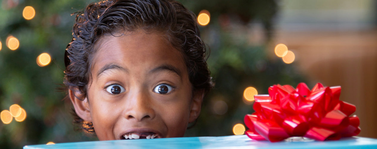 Elementary aged boy looks excited over the top of a stack of presents he's carrying.
