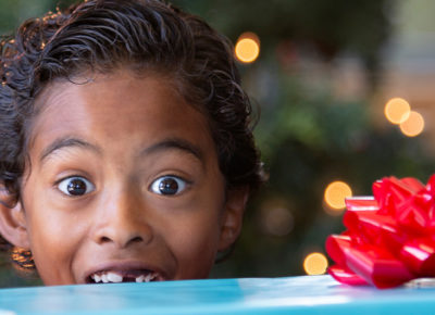 Elementary aged boy looks excited over the top of a stack of presents he's carrying.