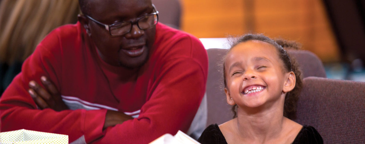 A dad sits next to his elementary-aged daughter, who has the biggest grin on her face.