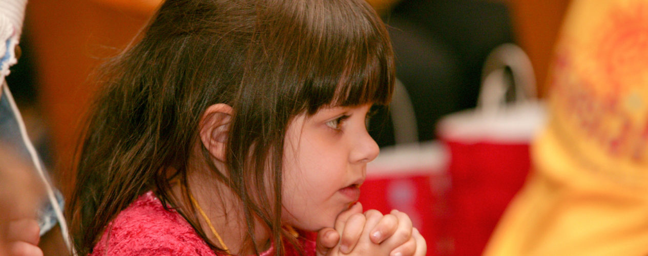Kindergarten girl prays with her hands by her chin.