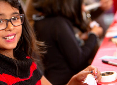 Elementary-aged girl in glasses participates in a craft at a table.