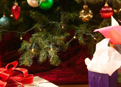 Gifts wrapped in boxes and bags with tissue paper sit beneath a decorated Christmas tree.