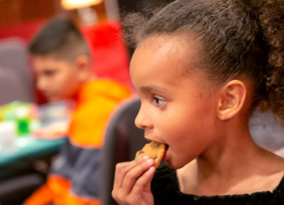 Elementary-aged girl eats a gingersnap cookie at her church Christmas party as she builds a crèche..