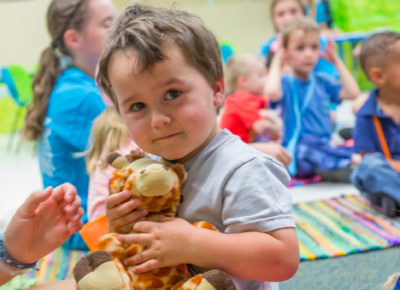 A preschool boy holding a stuffed giraffe.