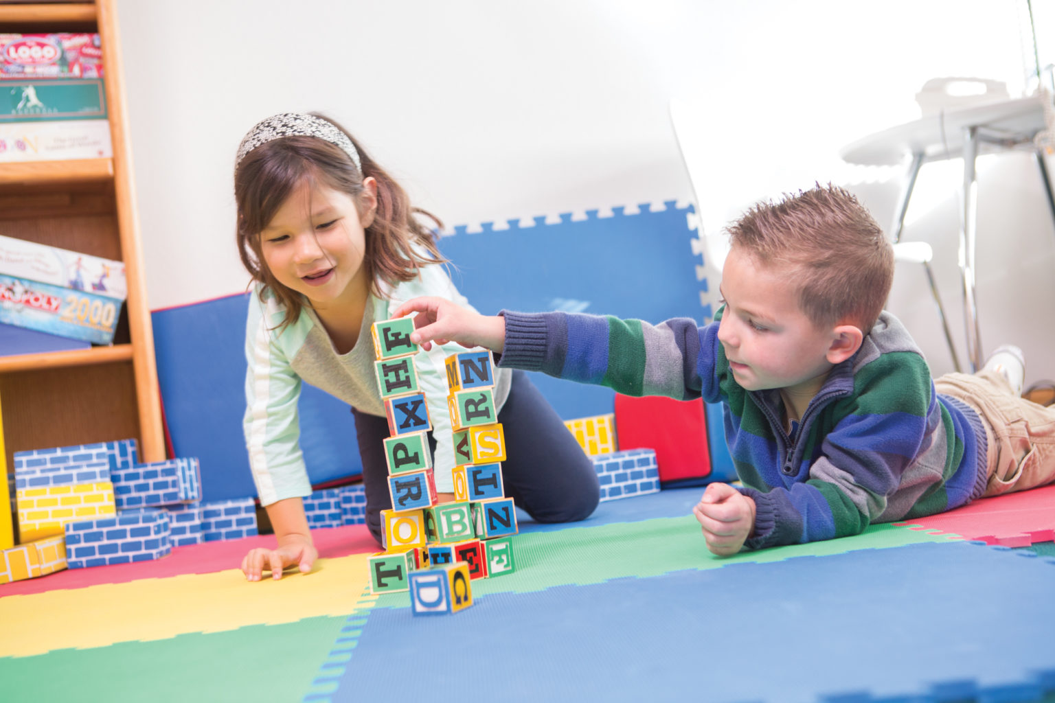 Two preschoolers play with blocks on a color mat.