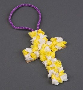 A yellow and white tissue paper cross with a purple hook to hang it on a door knob.