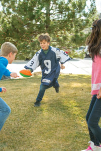 A boy in an green jersey runs to tag people with a football in his hands.