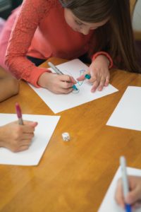 Four children sitting around a table, rolling a die and drawing something on a piece of paper.