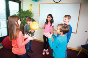 Five preteen children standing in a circle tossing around a mid-sized loaf of bread.