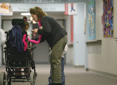 A mom stands in a hallway of a church helping her daughter who is in a wheel chair. Her son is standing next to her, as well.
