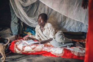 A teenage boy reading a Bible on his bed, with a mosquito net around him.