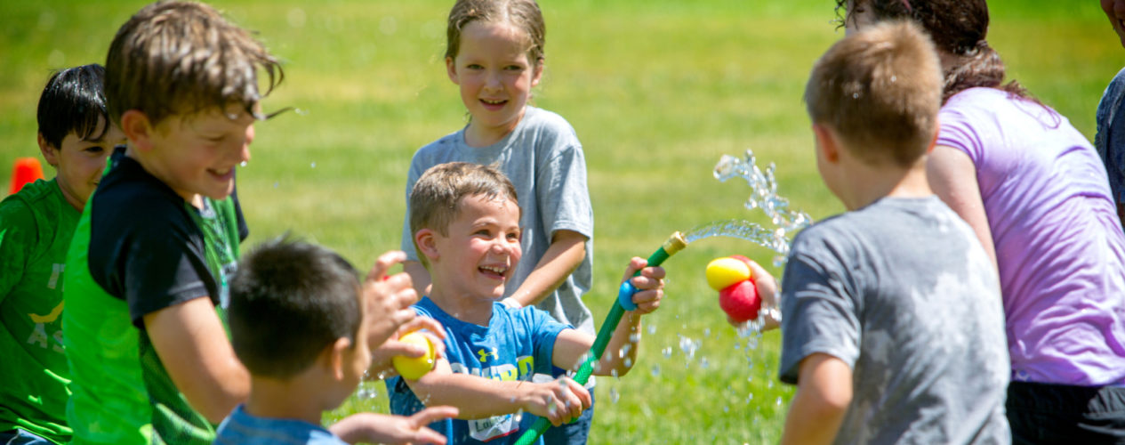 A group of kids are playing outside with a hose and some water balloons.