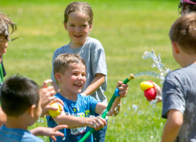 A group of kids are playing outside with a hose and some water balloons.