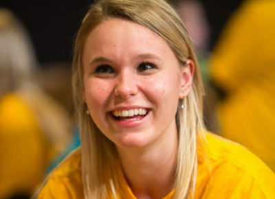 A female ministry leader in a bright yellow shirt smiles at the camera.