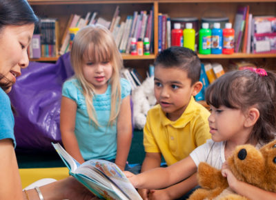 adult reading to three young kids in classroom