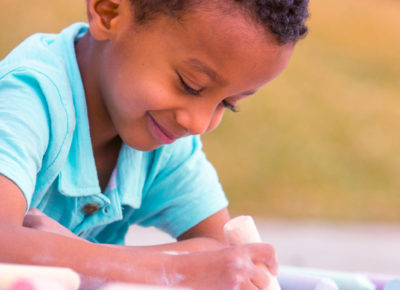 A preschool boy draws with chalk made from scratch from this money-saving list of ideas.