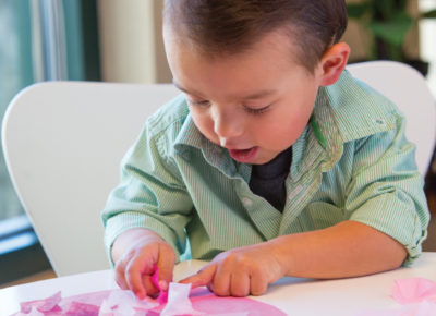 An older toddler is making a tissue paper heart. This idea appears on our list of nursery activity ideas.