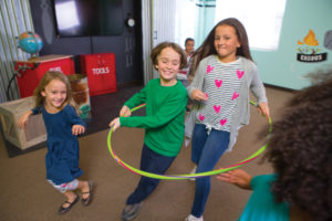 Two preteen children running together inside of a hula hoop. Other kids are running around them trying to not get tagged.