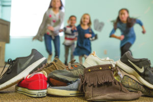 A pile of shoes with children running towards the pile.