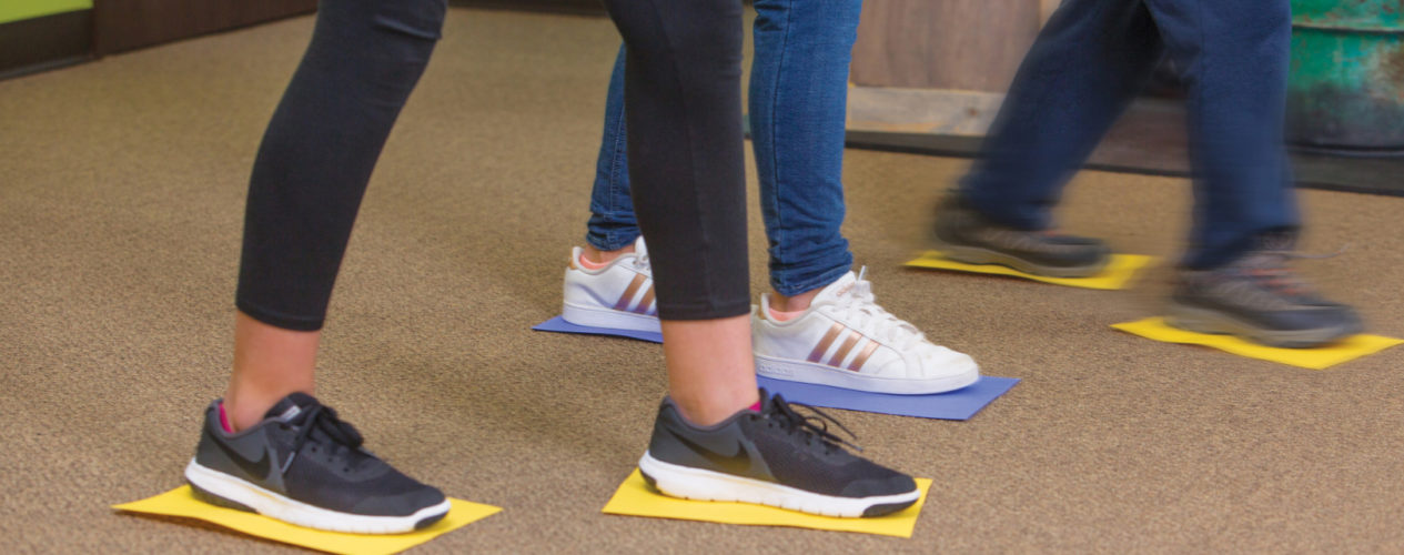A group of preteens shuffling across the ground with their shoes on a piece of construction paper. They are participating in the Paper Shuffle Bible-based activity for preteens..