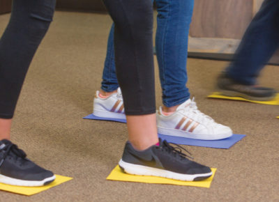 A group of preteens shuffling across the ground with their shoes on a piece of construction paper. They are participating in the Paper Shuffle Bible-based activity for preteens..